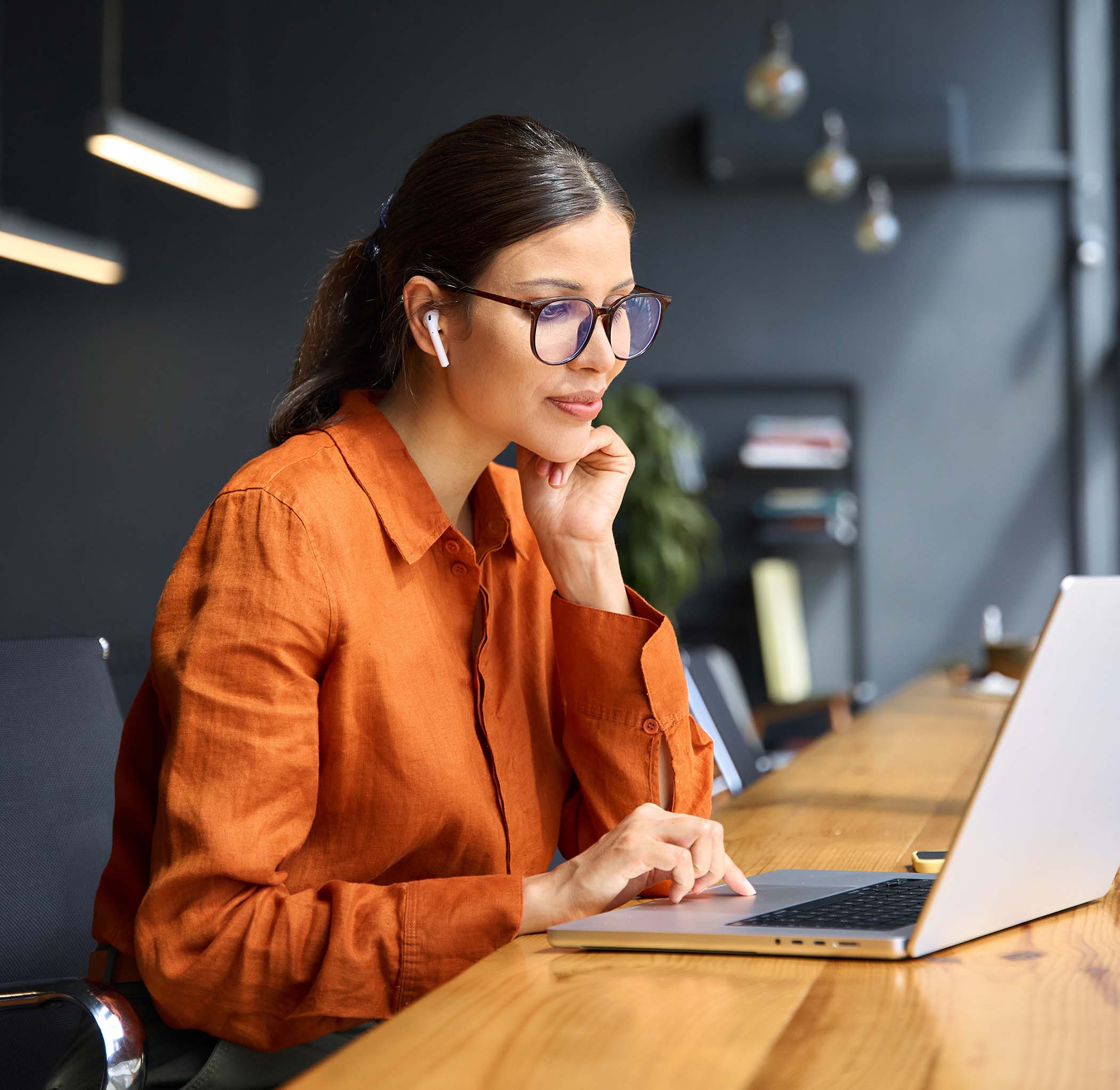 Busy latin hispanic young business woman working on laptop computer sitting at office desk. Indian entrepreneur manager businesswoman using pc for communication, learning at workplace. Vertical